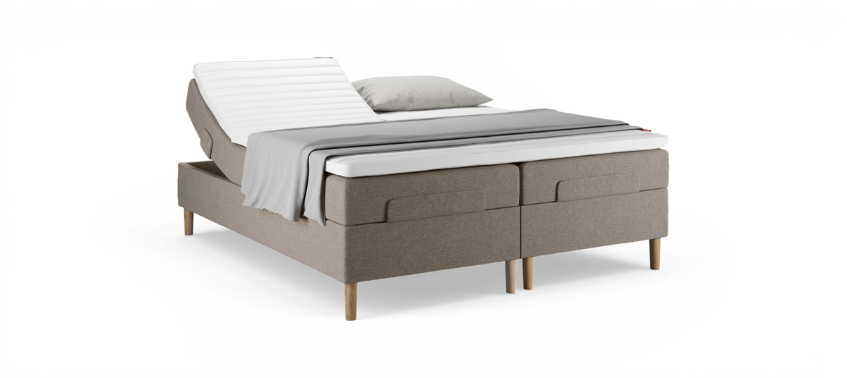 Justerbar dobbeltseng med hævet hovedende, beige polstret base, hvid topmadras samt gråt plaid og pude.