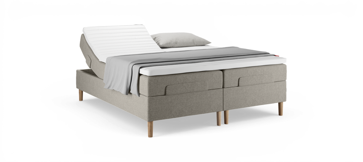 Beige elevationsseng med hævet rygdel, træben, hvid topmadras, gråt plaid og pude på hvid baggrund.