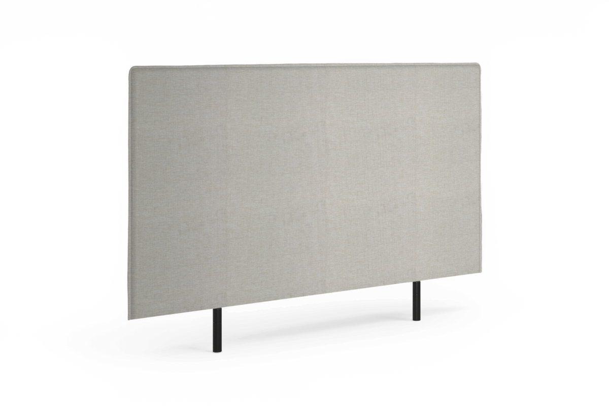 Beige, rektangulær sengegavl i stof med sorte ben, set i skrå vinkel.