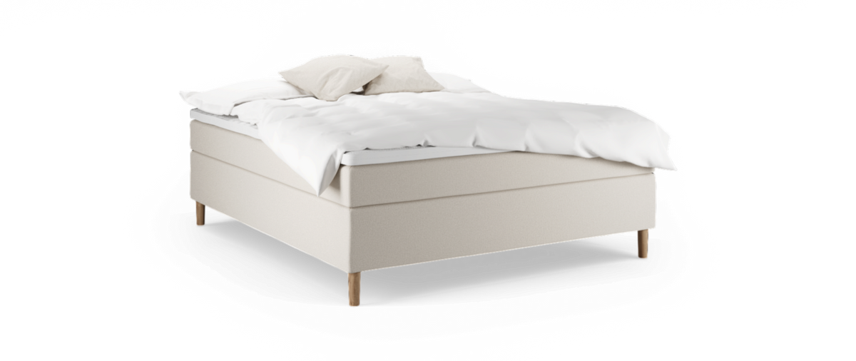 Beige seng med hvid opredning og to lyse puder på træben, fritlagt mod sort baggrund.
