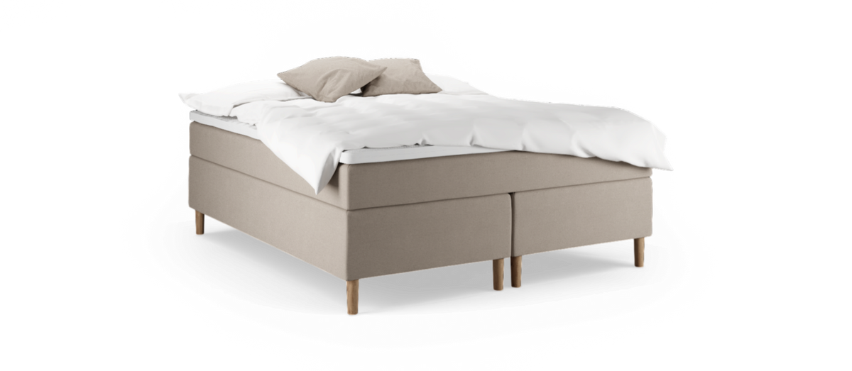Beige kontinentalseng med træben, hvid topmadras og to beige puder.