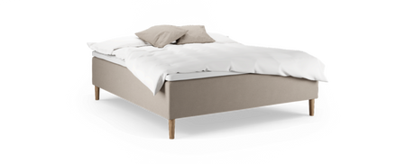 Beige polstret seng med træben, hvid dyne og to beige puder, fritlagt på sort baggrund.