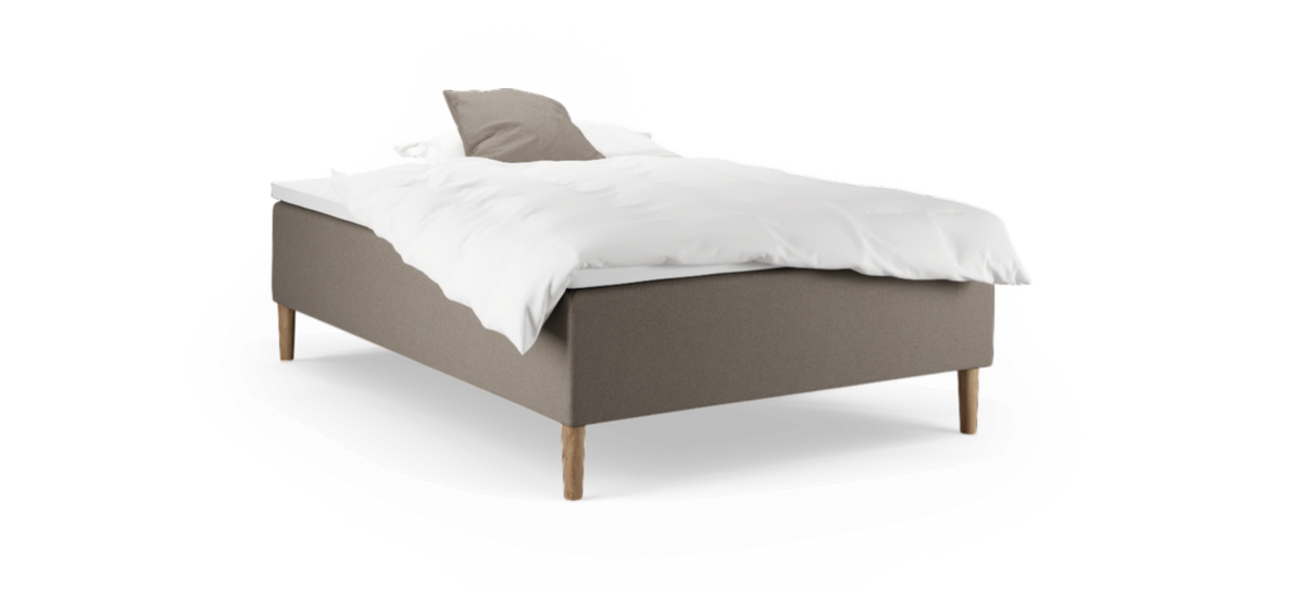 En enkeltseng med beige polstring, hvidt sengetøj og træben, fotograferet skråt forfra mod sort baggrund.