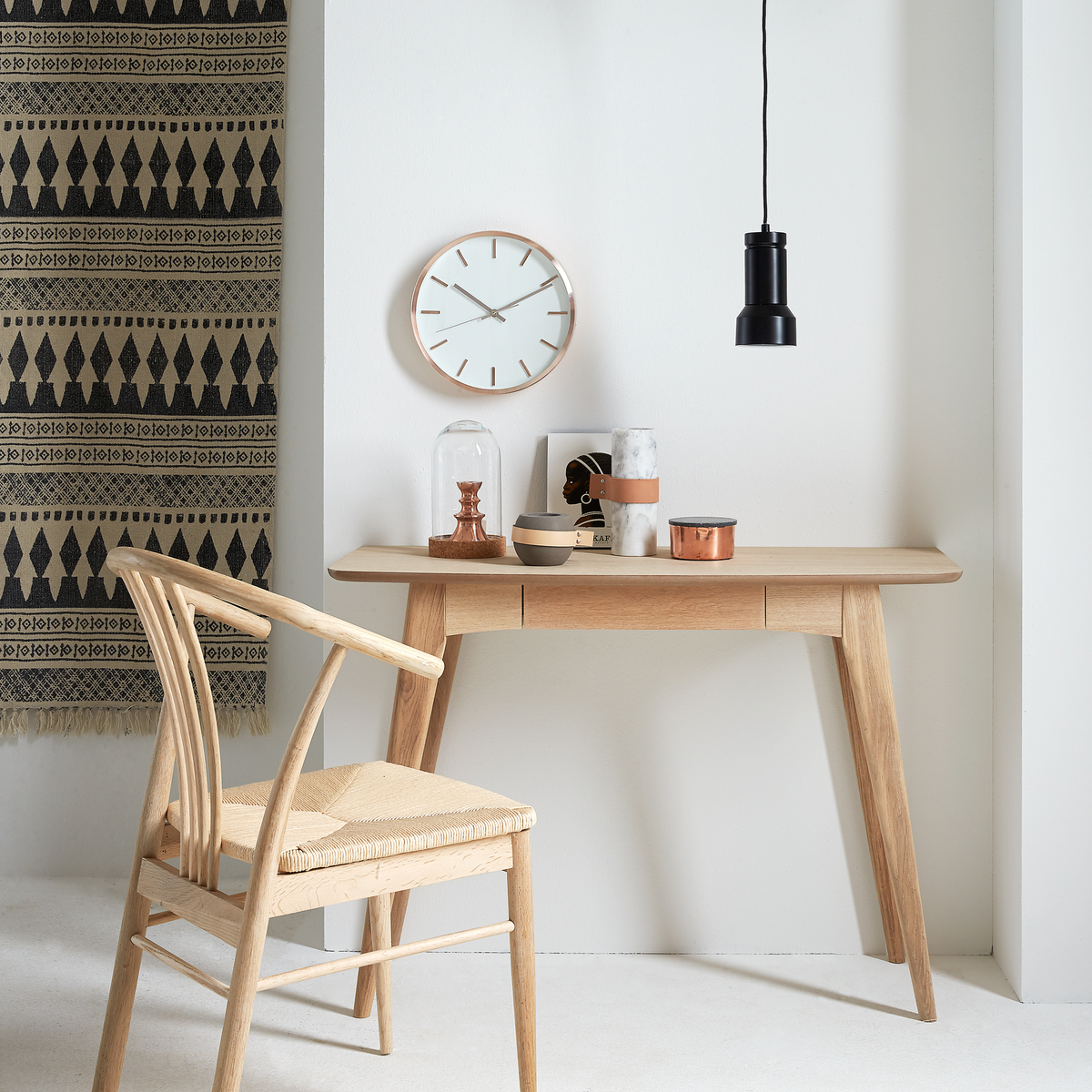 Lyst træskrivebord med stol, vægur og sort pendellampe i et skandinavisk, minimalistisk setup.
