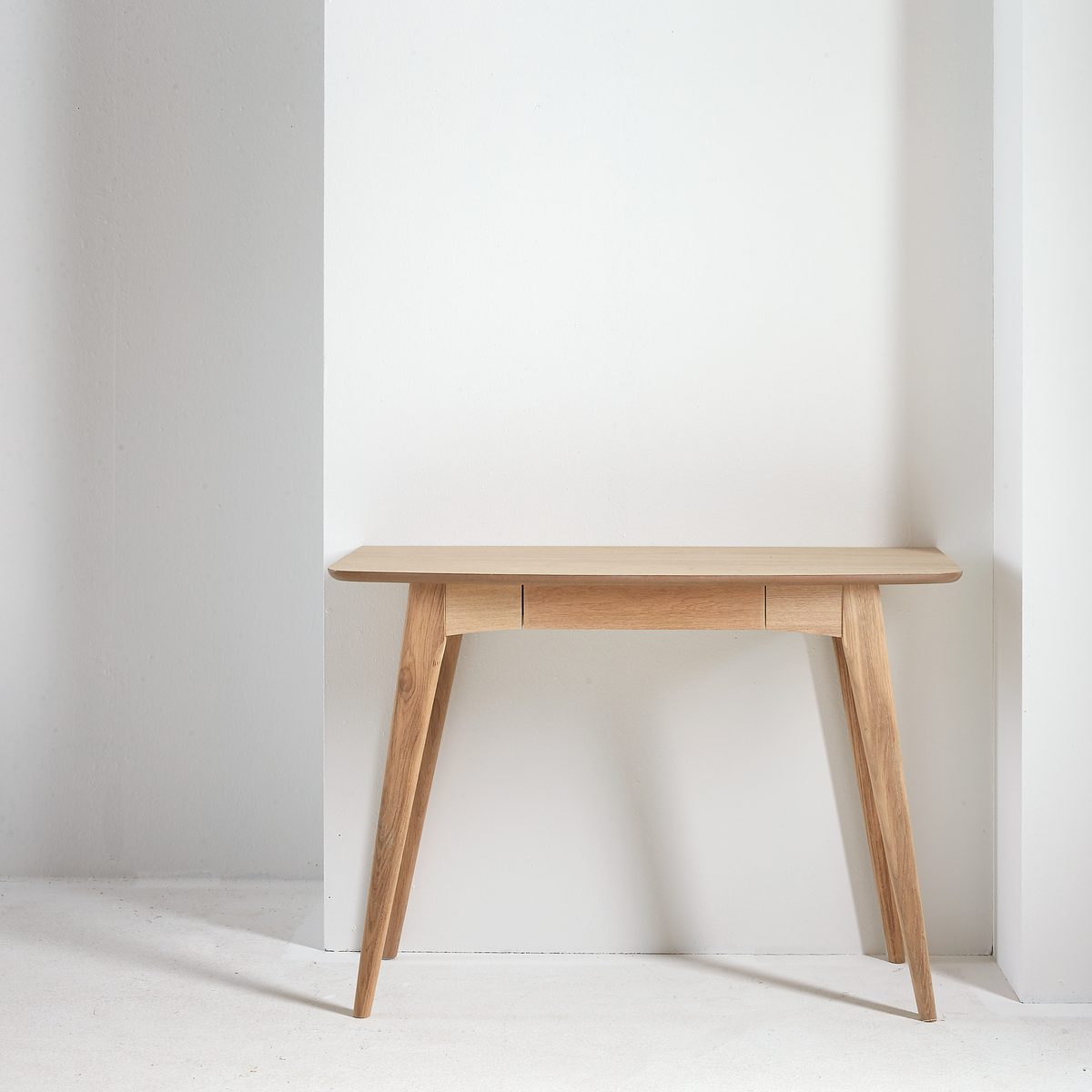 Konsolbord i lyst træ med tilspidsede ben mod en hvid, minimalistisk væg.