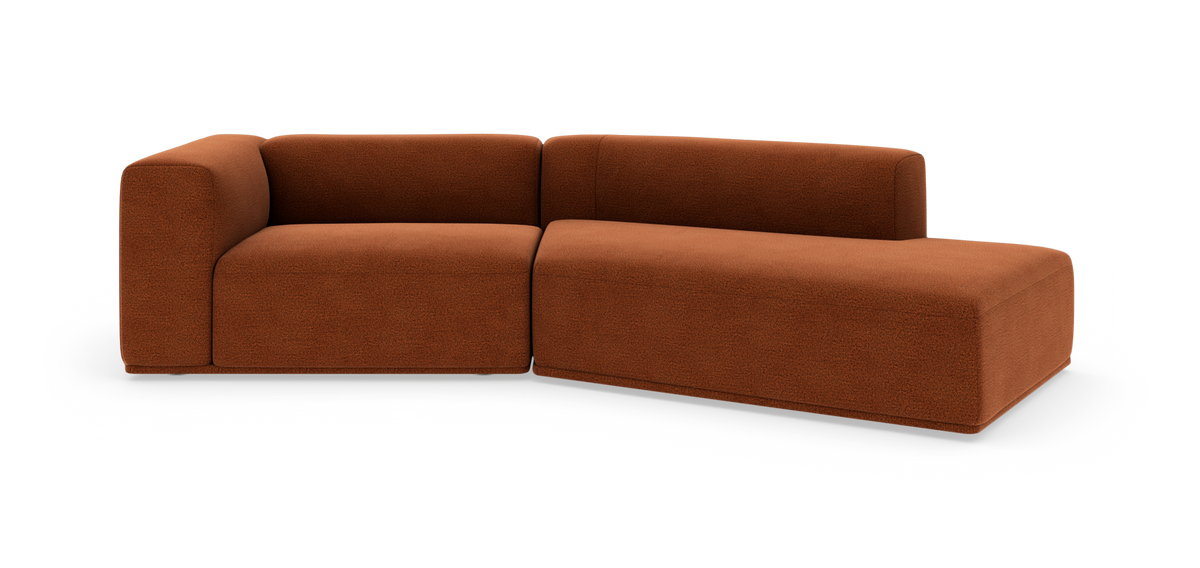 Modulær L‑formet sofa i rustrød tekstil med afrundede hjørner og lav ryg, frilagt på hvid baggrund.
