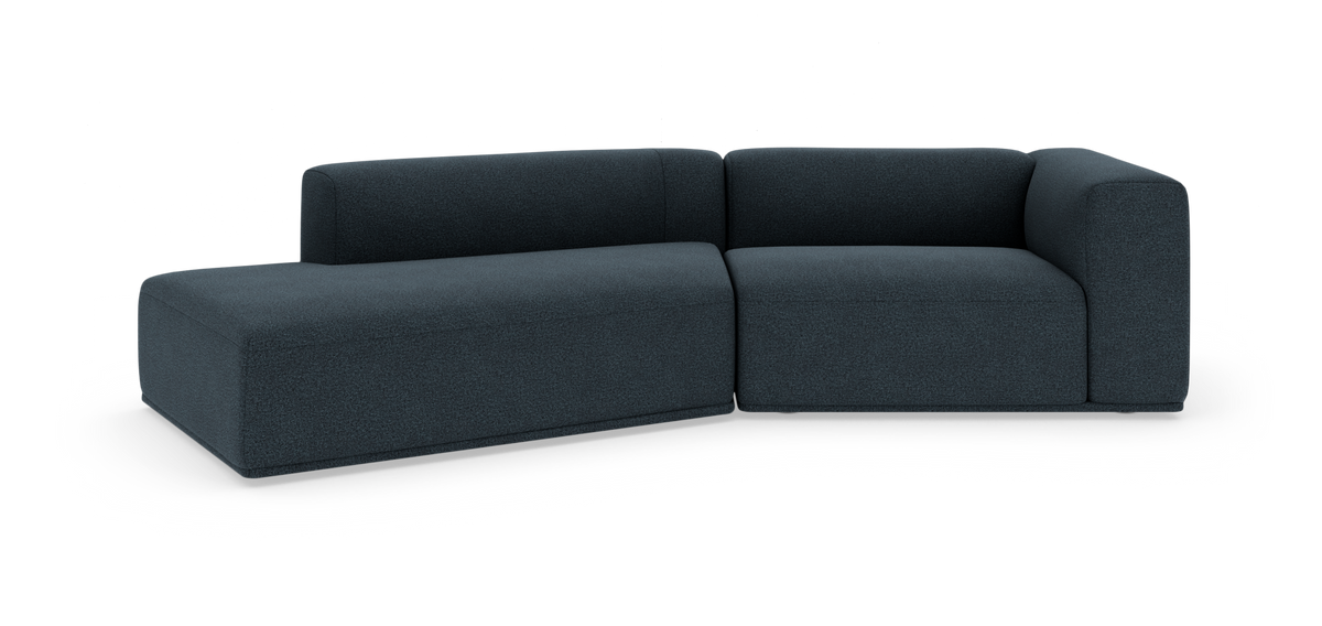 Mørkeblå modulsofa i L‑form med afrundede hjørner og lav ryg, frilagt på hvid baggrund.