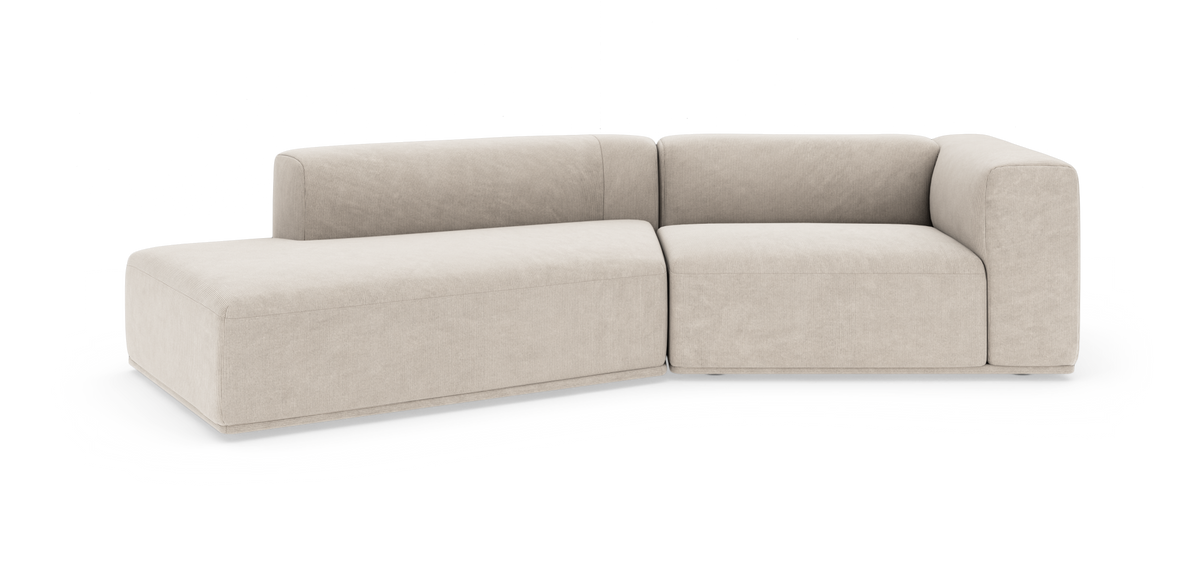Beige modulsofa i L-form med venstre chaiselong, bløde, blokformede linjer, fritstående på hvid baggrund.