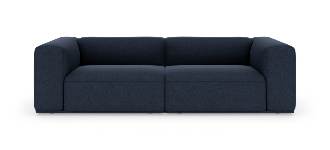Mørkeblå, moderne modulsofa med blødt afrundede armlæn, fotograferet lige forfra på hvid studiobaggrund.