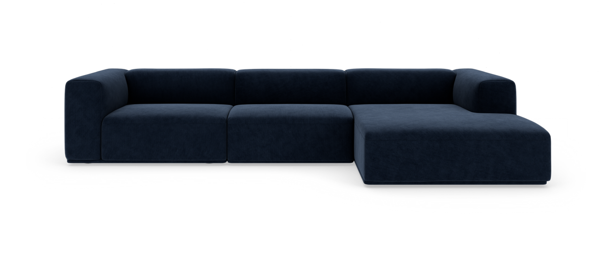 Modulsofa i mørk marineblå velour med højre chaiselong, set forfra på hvid baggrund.