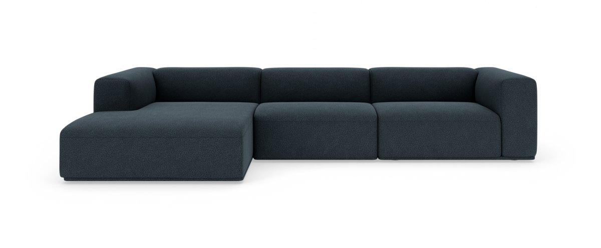 Mørkeblå modulsofa med chaiselong til venstre, lav med bløde, afrundede former, set forfra på hvid baggrund.